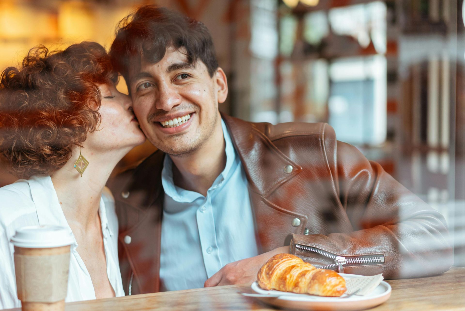 A joyful couple sharing a sweet moment in a cozy café setting, enjoying a croissant and coffee.