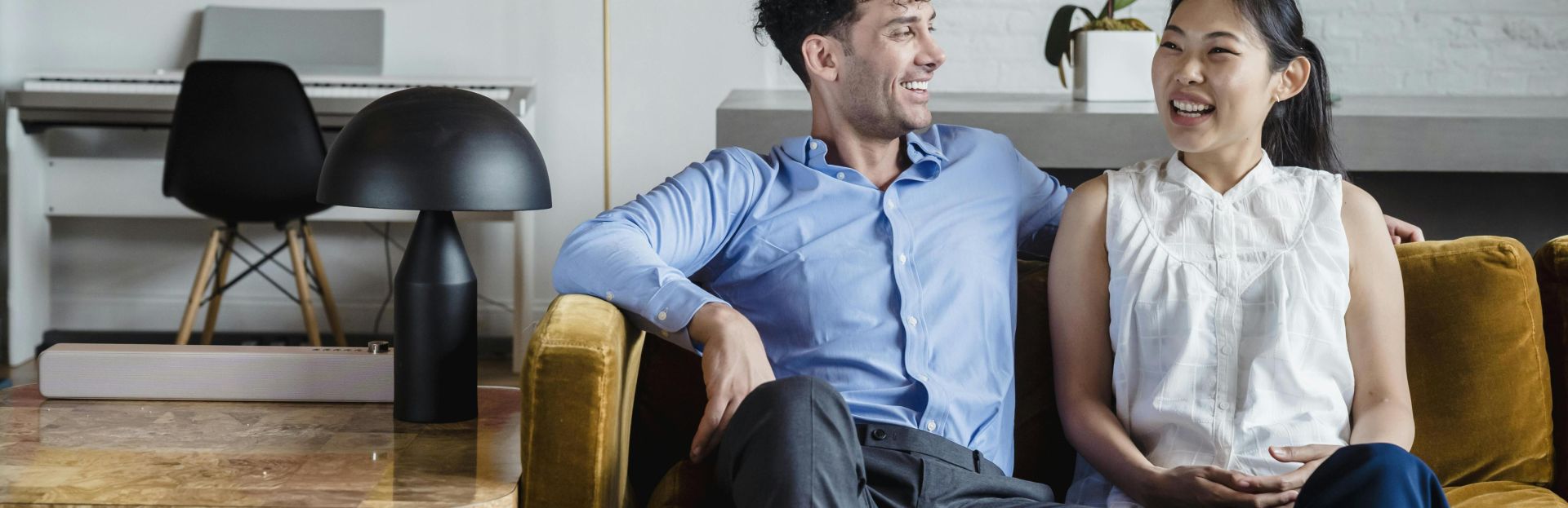 Asian woman and caucasian man laughing on a couch in a stylish living room setting.