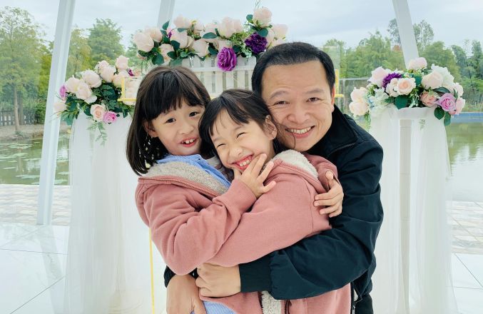 Father and daughters sharing joyful embraces and smiles in a floral setting.