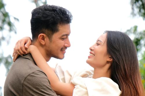 A couple embraces outdoors, showcasing romance and connection amidst lush greenery.