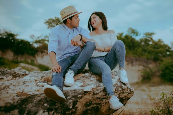 A happy couple sitting on a rock, sharing a joyful moment outdoors in nature.
