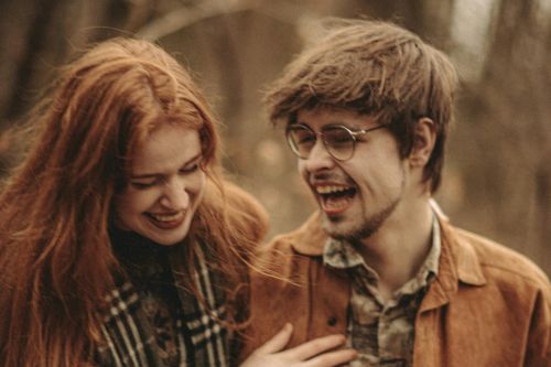 A happy couple laughing together in a serene autumn forest setting.