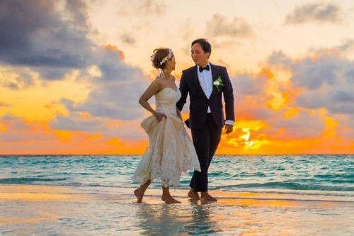 A young couple enjoying a romantic beach wedding during a vibrant sunset.