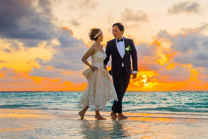 A young couple enjoying a romantic beach wedding during a vibrant sunset.